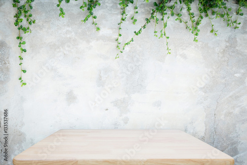 Wooden table with concrete wall and ornamental plants or ivy or garden tree for background.