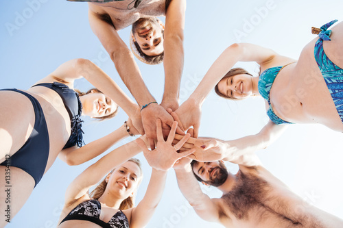 Group of friends in swimsuit on the beach with hands collected one above the other. View from below