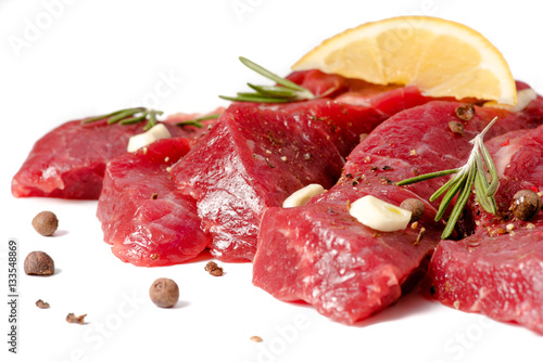 Pieces of meat with garlic, lemon and rosemary on wooden board isolated. Raw beef.