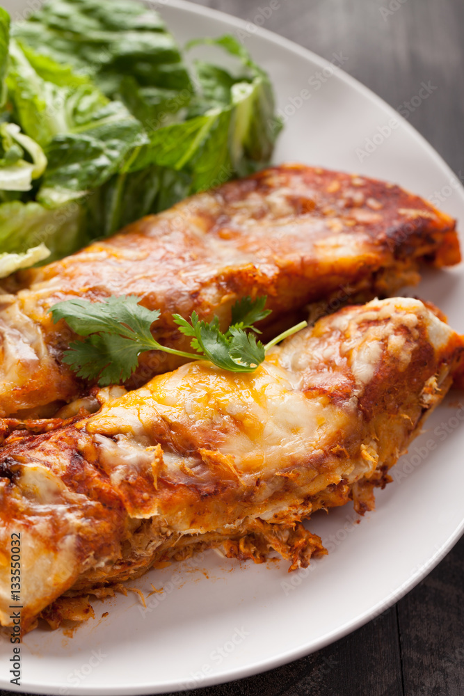 Spicy chicken enchiladas with a side of light green salad on a dark wood background close up shot