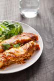 Spicy chicken enchiladas with a side of light green salad on a dark wood background 