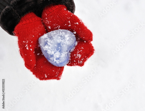 Female hands in knitted mittens with heart of blue ice in winter day. Love concept. Valentine day.