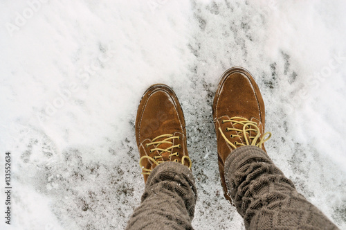 Female feet in shoes on the snowy pavement.