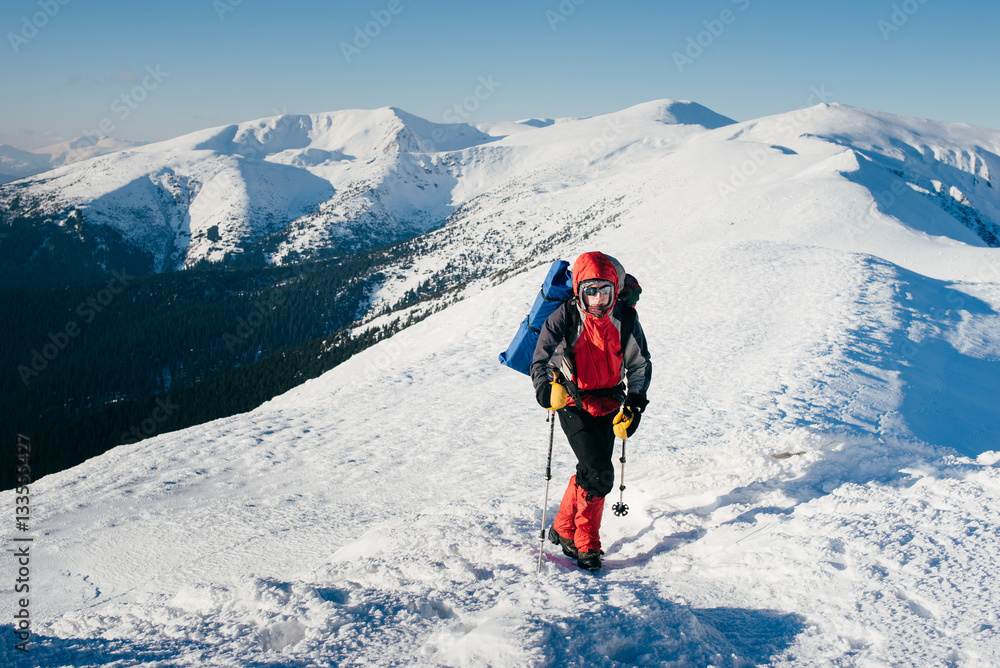 Man with backpack is hiking in snowy winter mountains