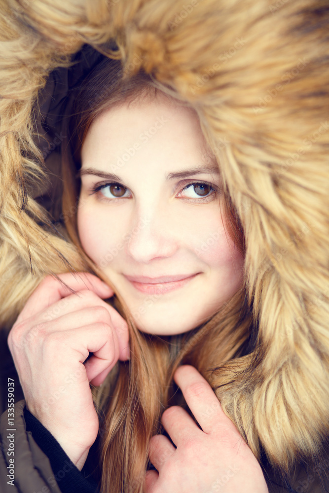 Young woman in fur hood. Close up portrait of beauty girl in winter park. Warm color toned image Young woman in fur hood. Close up portrait of beauty girl in winter park. Warm color toned image