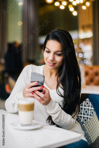 Young woman at cafe drinking coffee and using mobile phone 