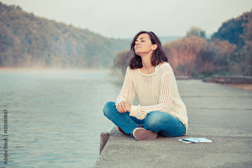 Relaxing. Woman sitting by lake taking brake from writing. 