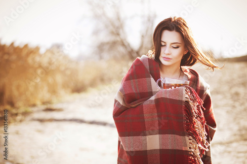 Beautiful sexy brunette sad woman in warm plaid at park with lake in cool weather