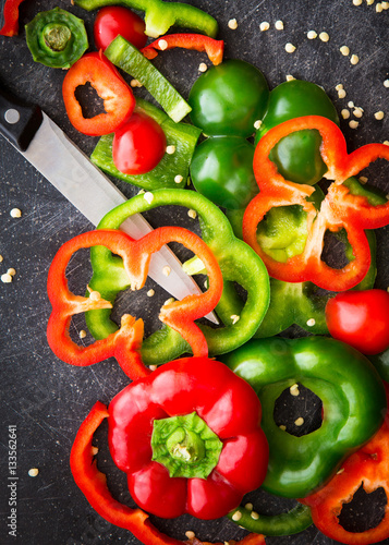 Cutting board and knife with fresh organic red and green bell peppers sliced and chopped for meal preparation. 