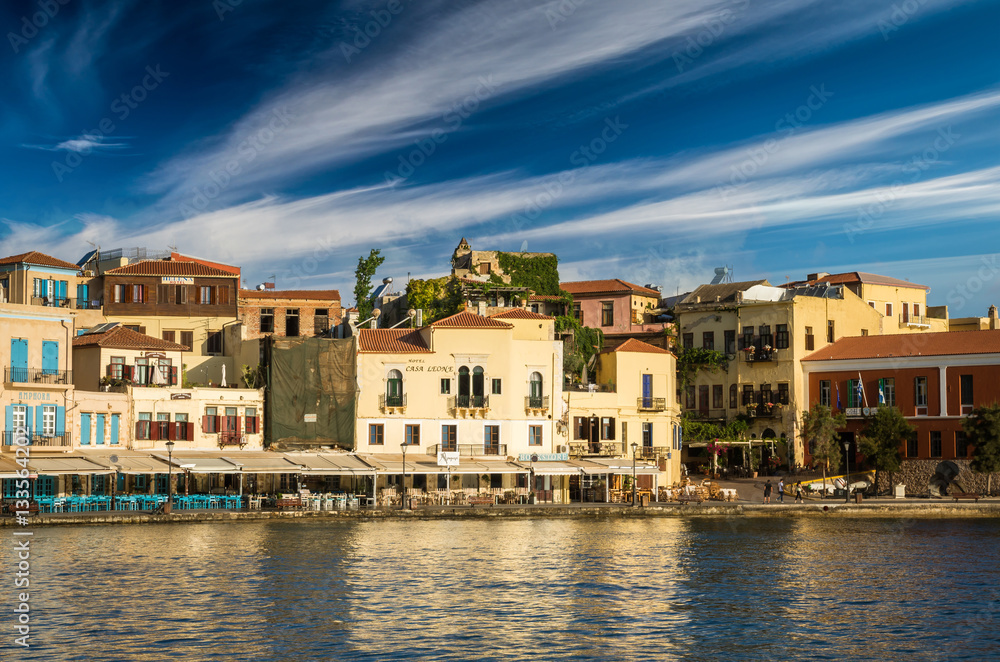 CHANIA, CRETE - JUNE 26, 2016: View of the old venetian port of Chania on Crete island, Greece. Tourists relaxing on promenade.