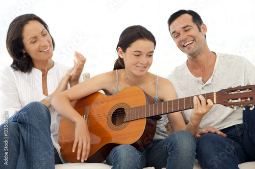 Family with one child having fun together when daughter plays music with guitar