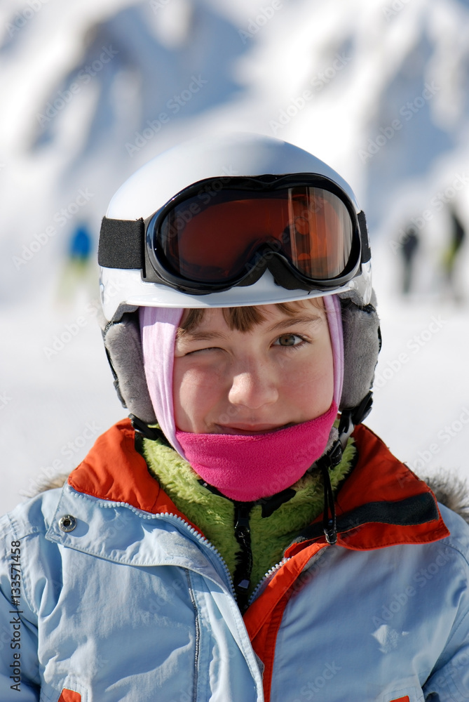 beautiful active smiling happy small young caucasian girl in helmet and ski jacket with ski googles during winter outdoor leisure recreat	