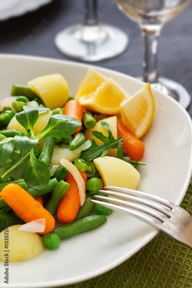 Salad with baby carrots, peas, onions and potatoes served on white plate on black wooden background