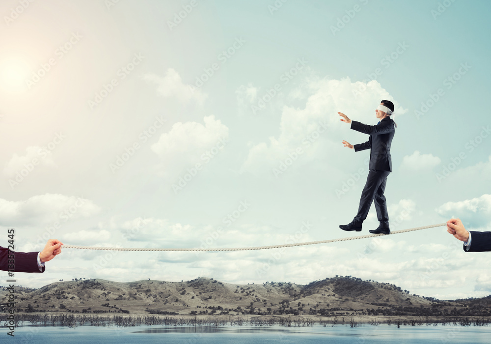 Business concept of risk support and assistance with man balancing on rope Business concept of risk support and assistance with man balancing on rope