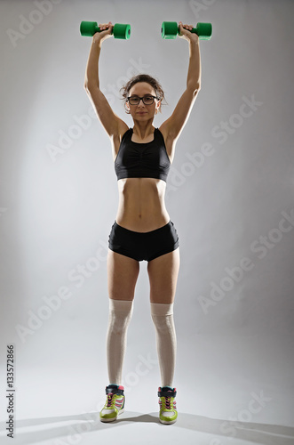 A slender young woman with a dumbbell on a gray background.