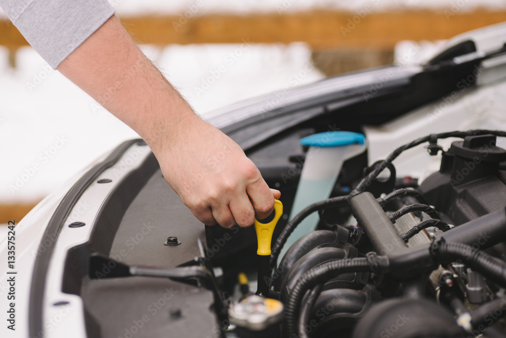 Car maintenance before winter. Man checking oil level in his car using dipstick. Outdoor closeup photograph Car maintenance before winter. Man checking oil level in his car using dipstick. Outdoor closeup photograph