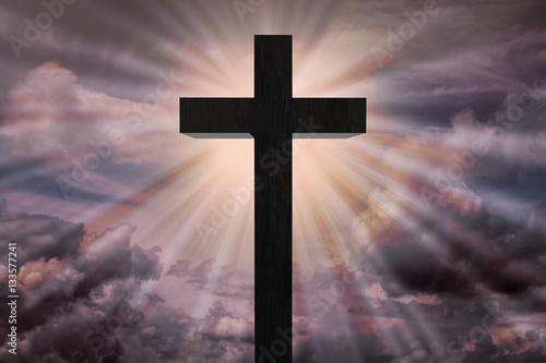 Jesus Christ cross on a sky with dramatic light, colorful sunset or sunrise, dark clouds, sun rays, sunbeams coming from behind the wooden cross. Easter, resurrection cross on a heavenly background  © maryd