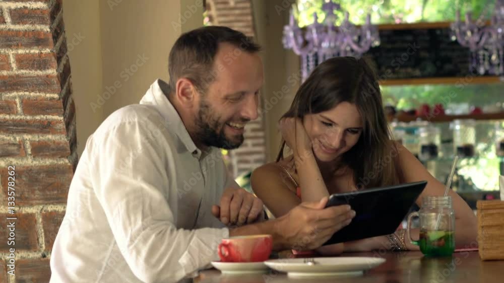 Happy, young couple talking and watching movie on tablet sitting by counter in cafe
Happy, young couple talking and watching movie on tablet sitting by counter in cafe