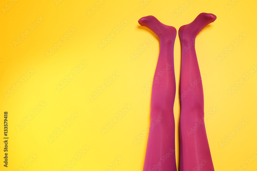 Beautiful woman legs in color tights on yellow background
