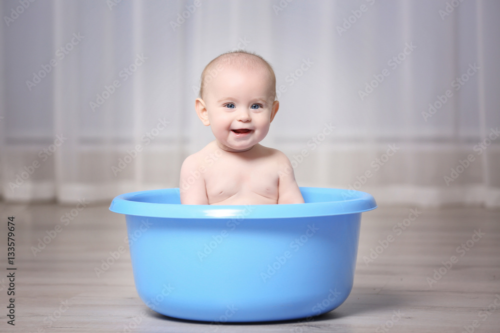 Cute baby in plastic basin at home