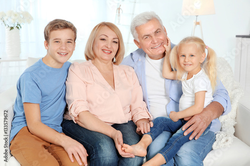Cute happy children with grandparents sitting on sofa in living room