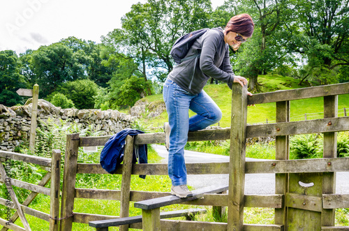 Woman Hiker Climbing Stile on a Path through the Countyside on a Sunny Spring Day