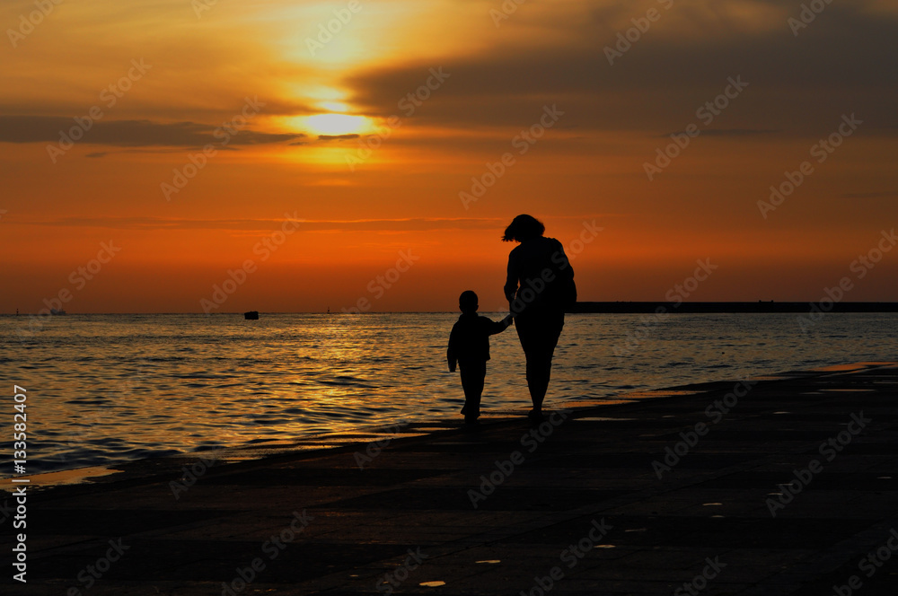 Woman with child holding hands run along the sea promenade