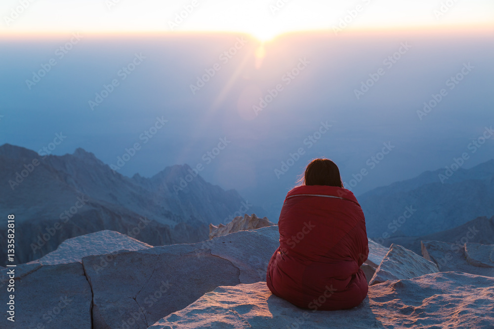 A young woman watches the sunrise from the top of a mountain