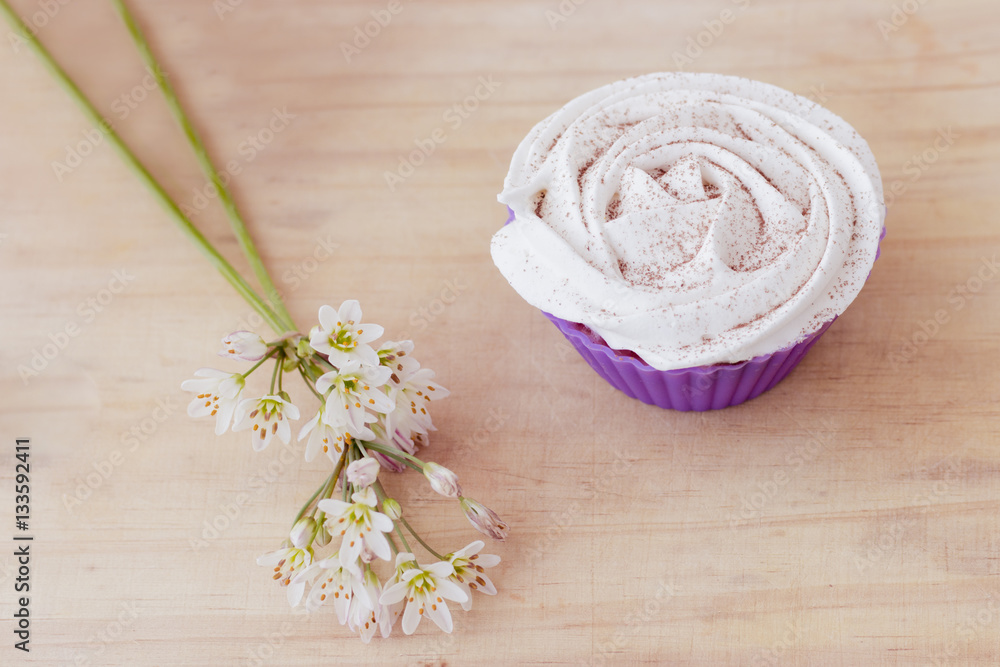 Vanilla cupcake with white frosting and flowers on a table Vanilla cupcake with white frosting and flowers on a table