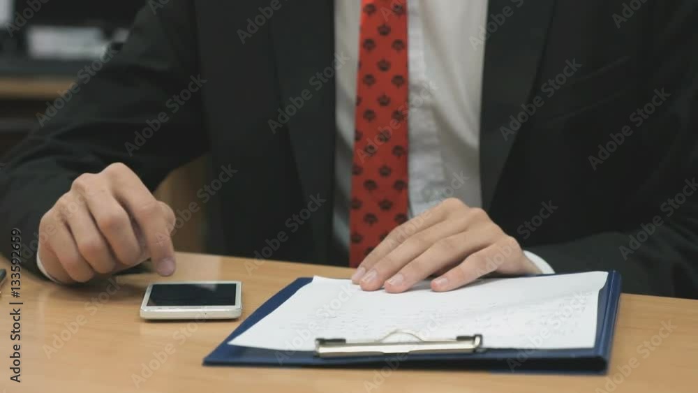Man sitting at the desk writing the text using the smartphone indoors Man sitting at the desk writing the text using the smartphone indoors