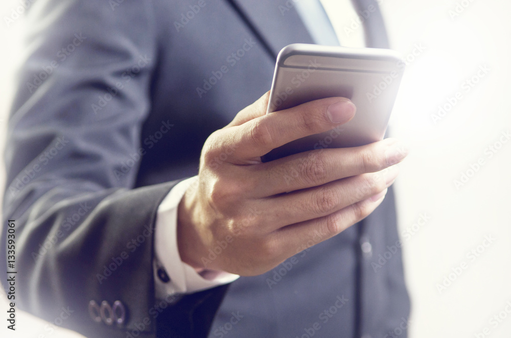 Close up of a business man using mobile smart phone with sunlight effect.