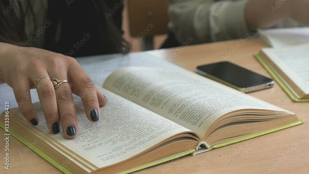The student sitting at the school desk flips the pages of the book The student sitting at the school desk flips the pages of the book