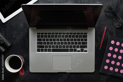 Laptop ,notebook, eyeglasses and other supplies  with cup of coffee . Black wooden desktop , top view .