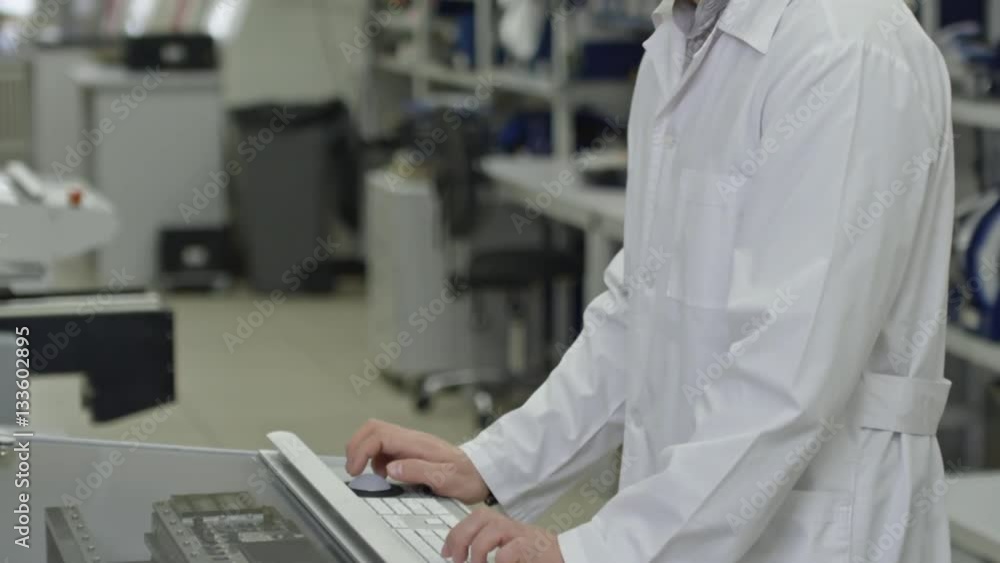 Tilt up of young Asian engineer in lab coat operating SMT machine at factory Tilt up of young Asian engineer in lab coat operating SMT machine at factory