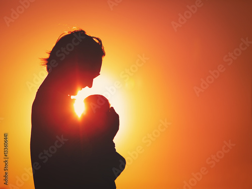 silhouettes of father and little newborn baby at sunset