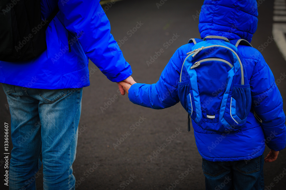 father holding hand of little son with backpack on road father holding hand of little son with backpack on road