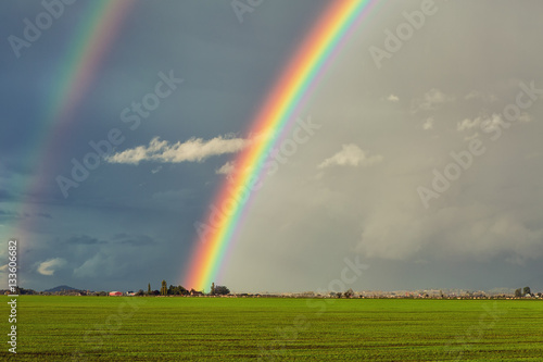 Big double rainbow over green field and red barn