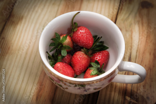 Strawberry fresh berries in white coffee cup on a wooden table.