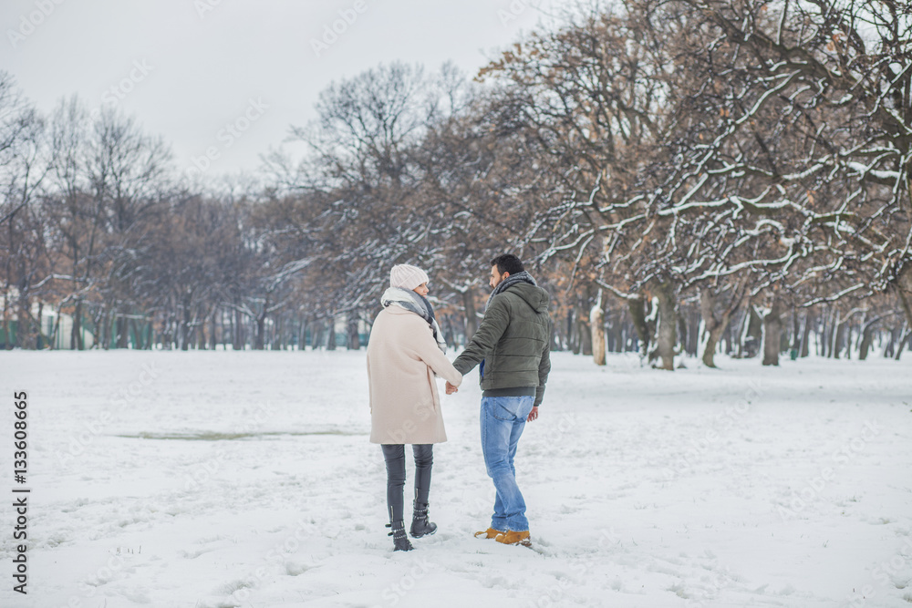 Happy loving couple walking in winter park enjoying snow