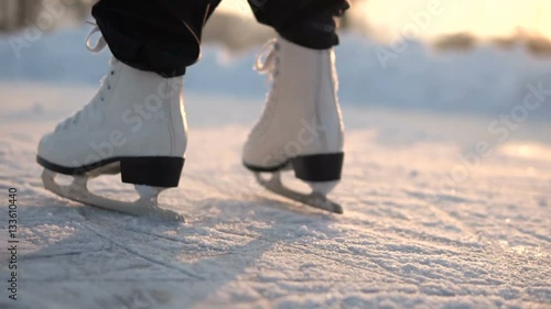 Low section of kid feet ice skating on frozen lake in sunny day