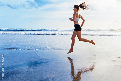 Obraz na plátně Active sporty woman run along ocean surf by water pool to keep fit and health