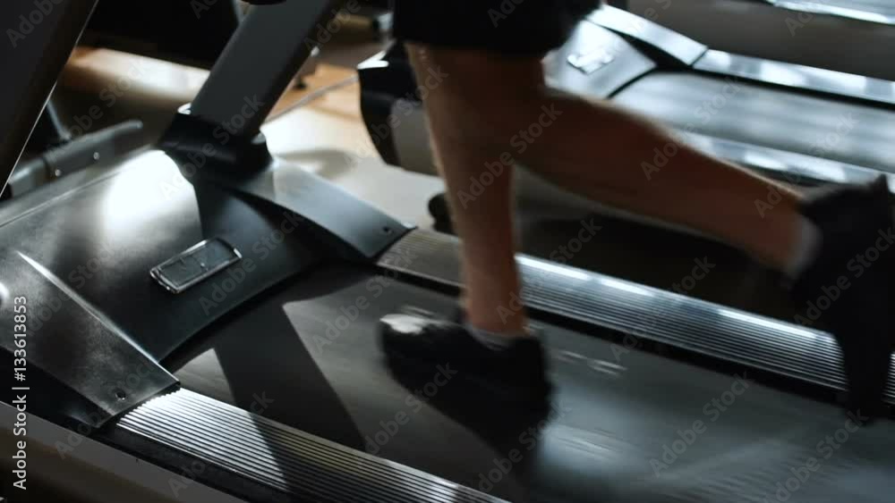 Side view of a young concentrated man in sportswear running on treadmill at gym Side view of a young concentrated man in sportswear running on treadmill at gym