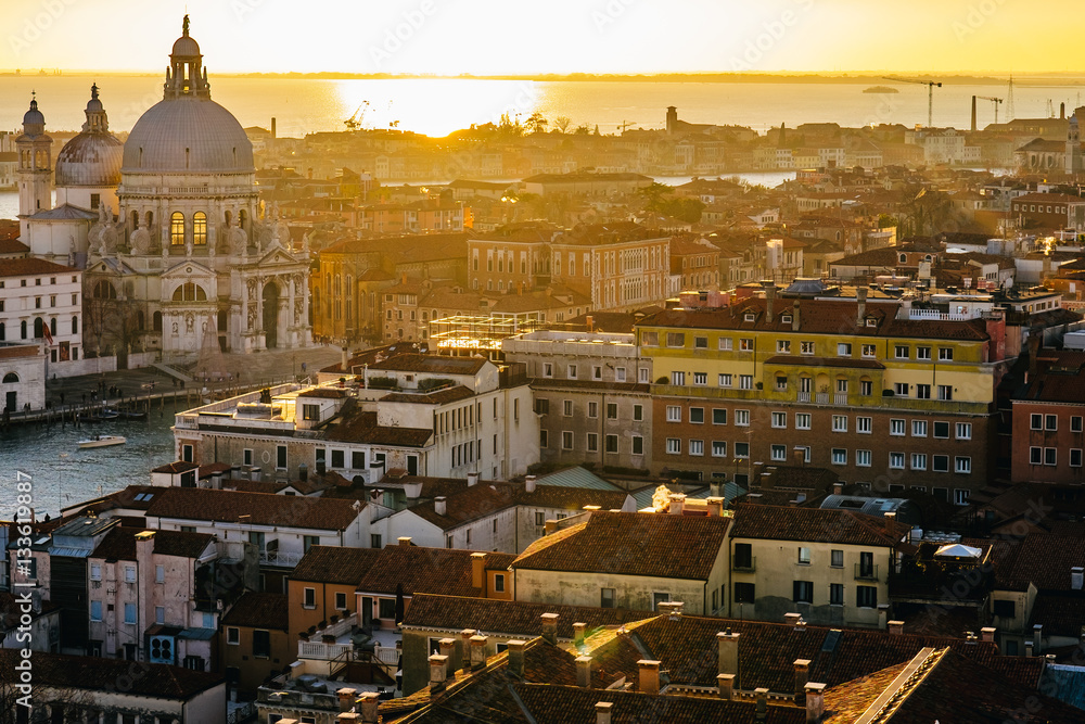 Fototapeta premium Aerial view of Venice, Italy, at sunset with rooftops of buildings and warm sunlight.