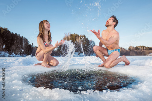 Young couple having fun and splashing the water of a winter lake