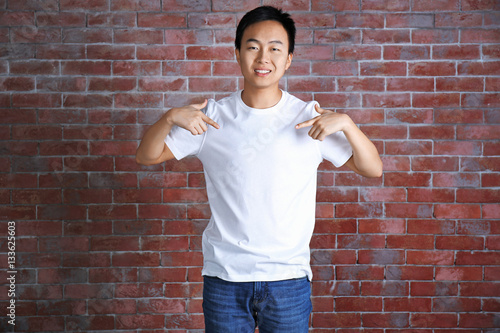 Asian man in blank white t-shirt standing against brick wall