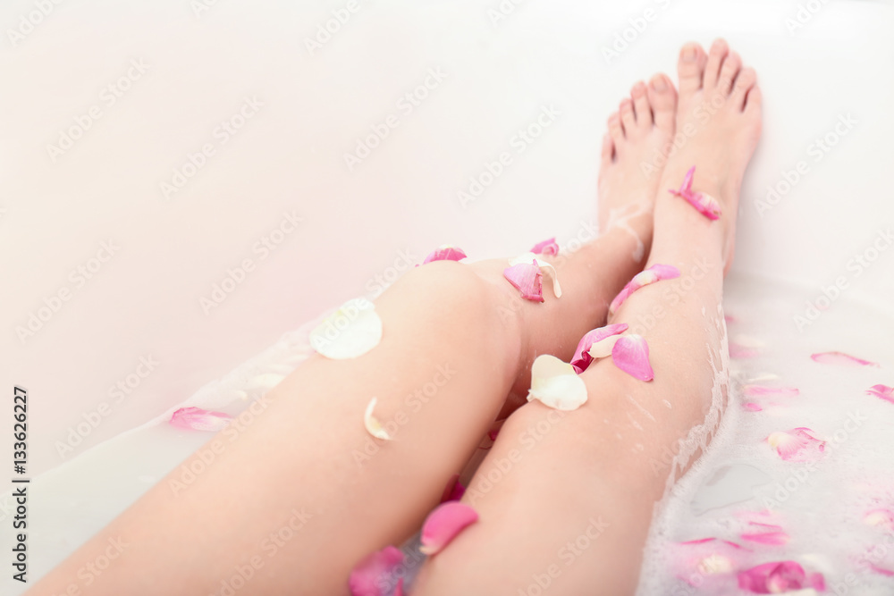 Woman relaxing in bath with foam and petals, closeup of female legs Woman relaxing in bath with foam and petals, closeup of female legs