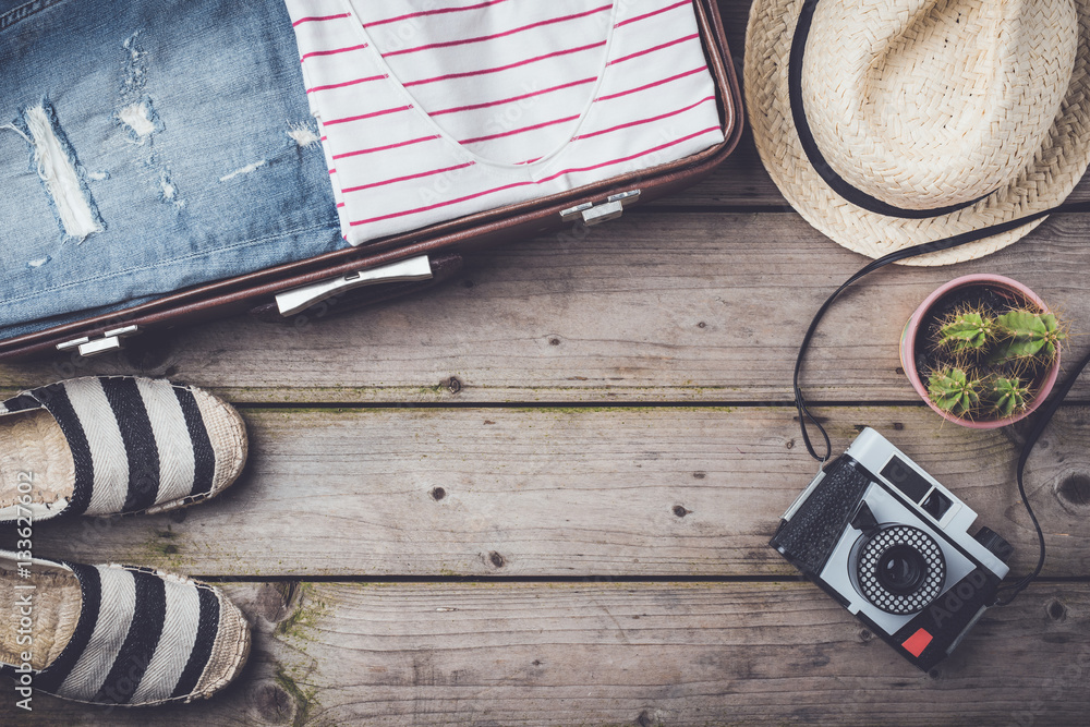 Fototapeta premium Travel preparations concept with suitcase, clothes and accessories on an old wooden table. Top view
