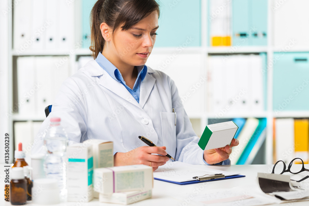 Female pharmacist sat at desk writing notes Female pharmacist sat at desk writing notes