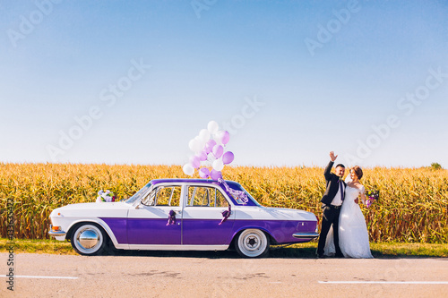 Obraz na płótnie Stylish Loving wedding couple kissing with baloons and hugging on nature near retro car w salonie