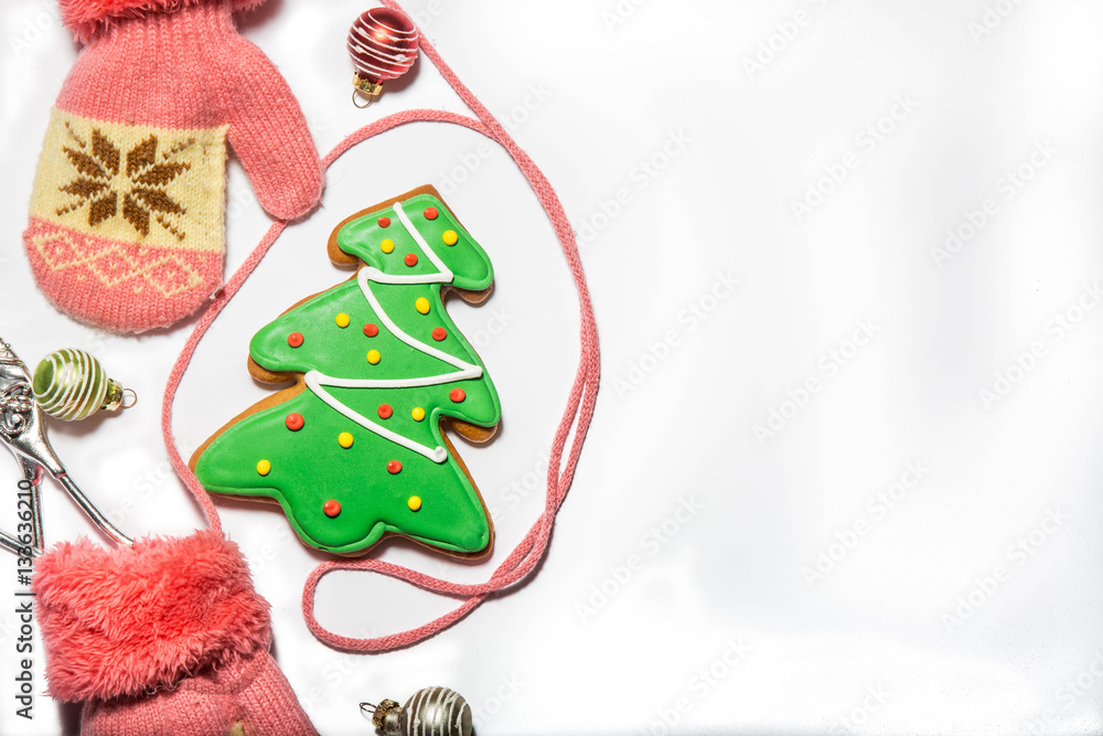 gingerbread in the shape of Christmas trees, Christmas decorations and baby pink knitted mittens on a string on white background